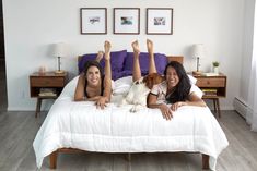 two women laying on a bed with a dog in front of them and their legs up