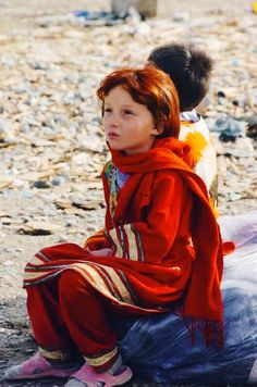 a young boy sitting on top of a plastic bag next to another child in the background