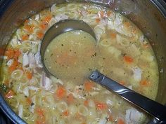 a pot filled with chicken noodle soup and a ladle on the stove top