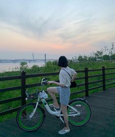 a woman riding a bike on top of a wooden deck next to a body of water