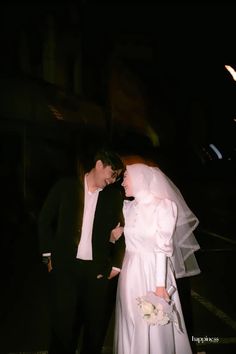 a bride and groom standing next to each other in front of a building at night