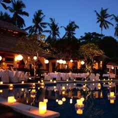 many lit candles are floating in the water near a pool with chairs and tables around it