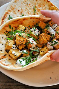 a hand holding a tortilla filled with tofu and spinach on top of a white plate