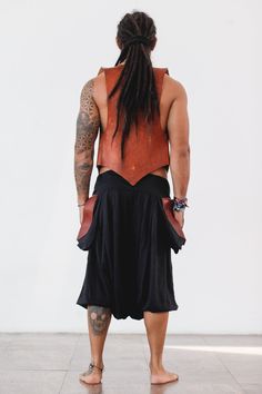 a man with dreadlocks standing in front of a white wall wearing a black skirt