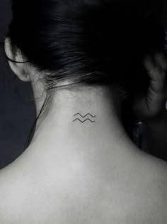 the back of a woman's neck with a small wave tattoo on it