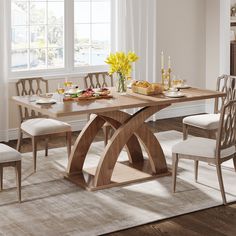 a wooden table with chairs around it in front of a white rug and large windows