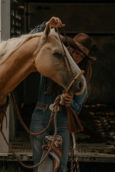 a woman in jeans and cowboy hat standing next to a brown horse with rope around it's neck