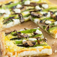 a pizza with asparagus, mushrooms and feta cheese is cut in half