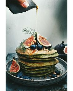 a stack of pancakes with blueberries and figs being drizzled with syrup