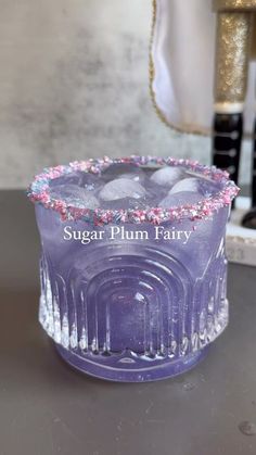 a purple cake sitting on top of a table next to a glass vase with pink and blue sprinkles