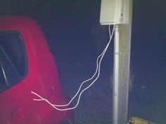 a red car parked next to a pole with an electrical outlet on it's side