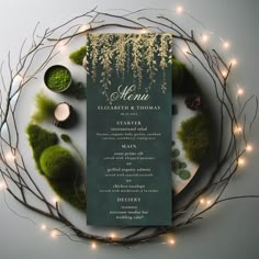 a green menu card surrounded by greenery and lite - up candles on a white plate