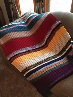 a multicolored blanket sitting on top of a couch in front of a window