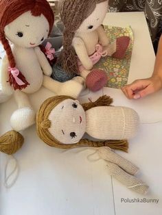 three knitted dolls sitting on top of a table next to yarn balls and thread