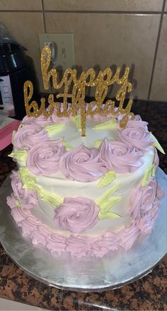 a birthday cake with pink and yellow frosting roses on it, sitting on a counter