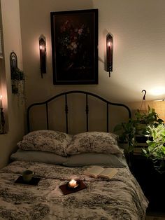 a lit candle on a bed in a dimly lit room with two plants and books