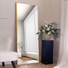 a mirror sitting on top of a wooden floor next to a vase with flowers in it