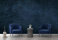 two blue chairs sitting next to each other in front of a wall with a vase on it