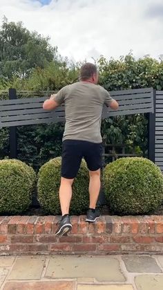 a man standing on the edge of a brick wall next to bushes and shrubbery