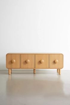 a wooden cabinet with four drawers and three knobs on each drawer, in front of a white wall