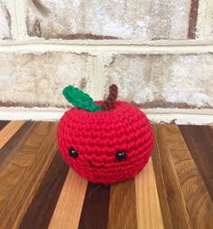 a crocheted red apple sitting on top of a wooden table next to a brick wall