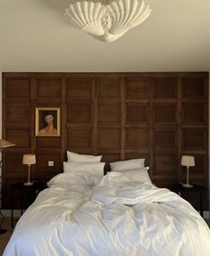 a bed with white sheets and pillows in a bedroom next to a painting on the wall