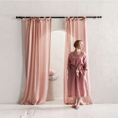 a woman standing in front of a window with pink drapes on the curtain rod