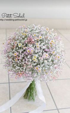 a bouquet of daisies and baby's breath tied to a white ribbon on a tiled floor