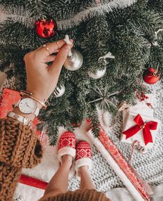 someone is decorating a christmas tree with red and white ornaments on it, while another person holds a watch in their hand