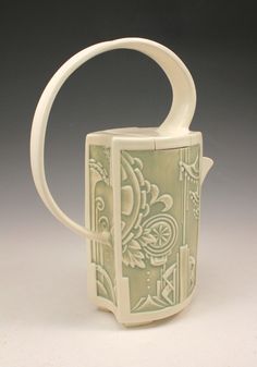 a white and green ceramic cup with an intricate design on it's side, in front of a gray background