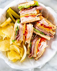 a sandwich and chips in a paper bowl on a marble counter top with a pickle