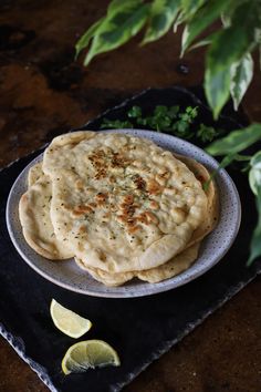 two pita breads on a plate with lemon wedges and parsley in the background