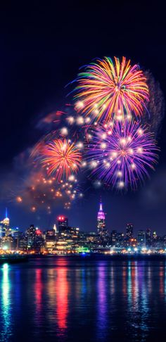 fireworks are lit up in the night sky over water and city buildings with lights on them