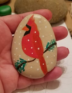 a hand holding a painted rock with a red bird on it