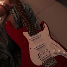 a person sitting on the floor with a red guitar in their lap and holding it up