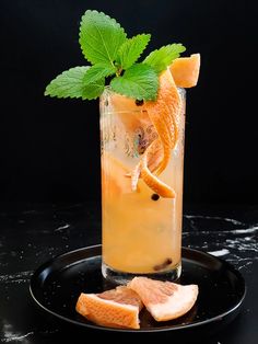 a drink with orange slices and mint garnish on a black plate next to it