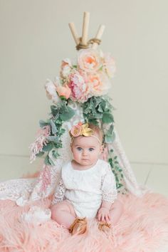 a baby is sitting on a pink rug with flowers and candles in the background, wearing a crown