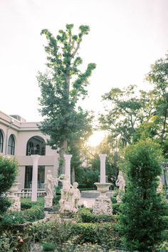 a garden with statues and trees in front of a large white house on a sunny day