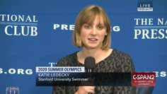 a woman speaking into a microphone in front of a blue wall with the words spring olympics written on it