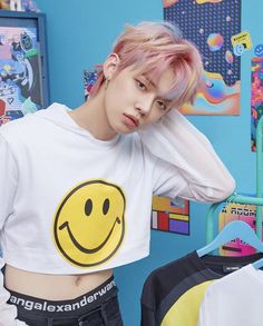 a young man with pink hair wearing a smiley face t - shirt in front of a blue wall