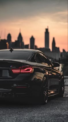 a black sports car parked in front of a cityscape at sunset or dawn