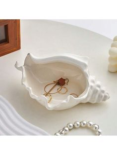 a white shell shaped jewelry box on a table next to pearls and a bead bracelet