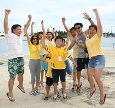 a group of people standing on top of a sandy beach next to the ocean with their arms in the air