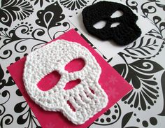 two crocheted masks are sitting on top of a pink and black paper towel