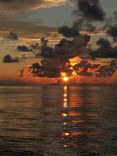 the sun is setting over the ocean with clouds in the sky and reflecting on the water