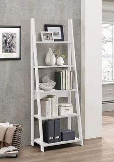 a white book shelf with books and pictures on the top, in front of a gray wall