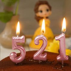 a birthday cake with candles in the shape of number twenty five and a doll behind it