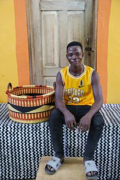 a young man sitting on top of a wooden bench in front of a basket and door