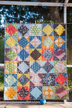 a colorful quilt hanging from a clothes line on the side of a building with trees in the background