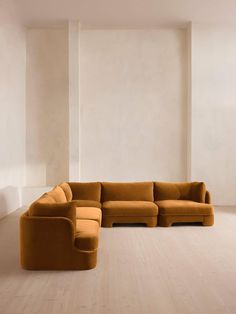 a large sectional couch in an empty room with white walls and wood flooring on the side